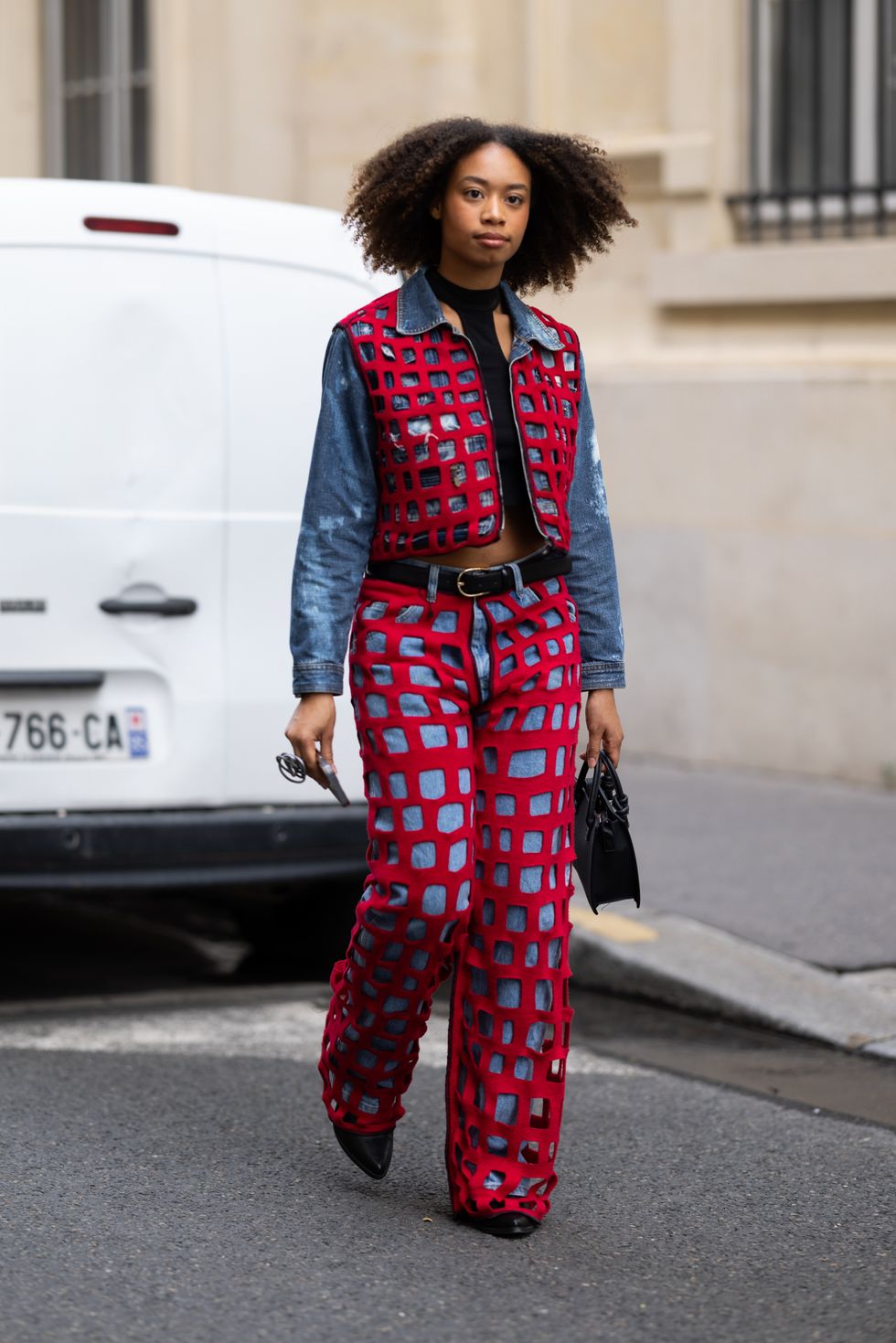 A guest is seen wearing black leather shoes, a black leather bag, a black belt, a black top and a red fishnet and blue jeans coord-set made of a cropped long sleeves jacket and high waist trousers outside the Marni show during the Womenswear Spring/Summer 2024 as part of Paris Fashion Week