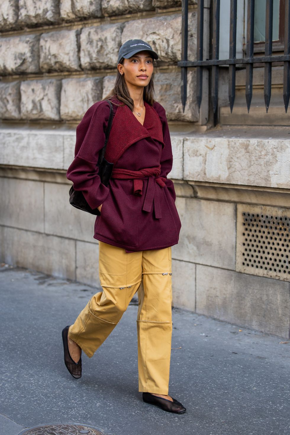 A guest wears cap, burgundy jacket, beige pants with side pockets outside Hermes during the Womenswear Spring/Summer 2024 as part of Paris Fashion Week