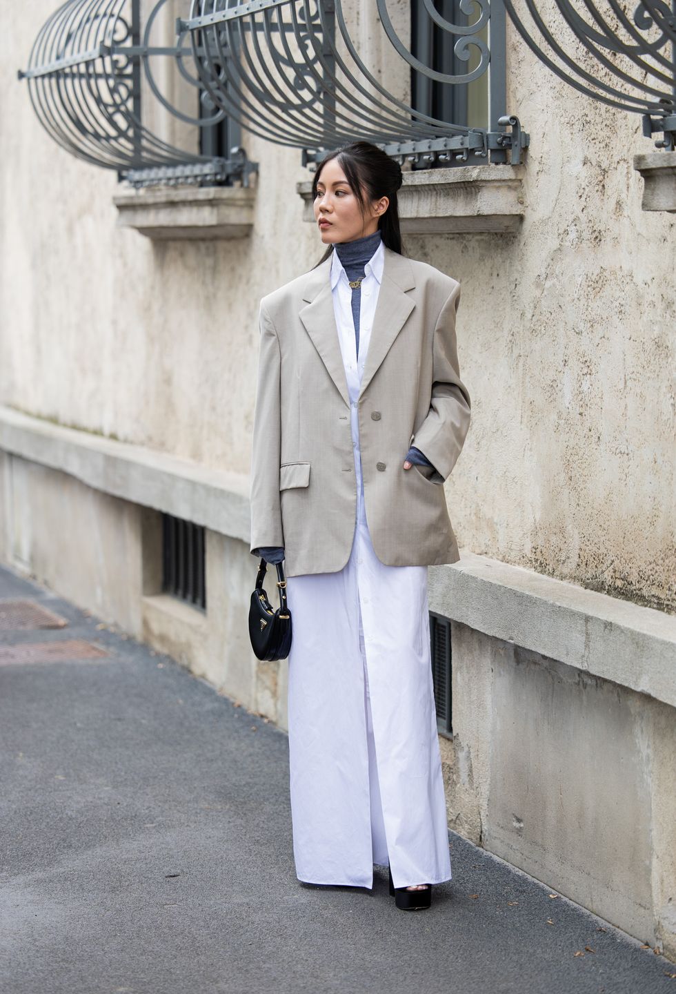 A guest wears grey oversized blazer, white long button shirt, black bag outside Prada during the Milan Fashion Week