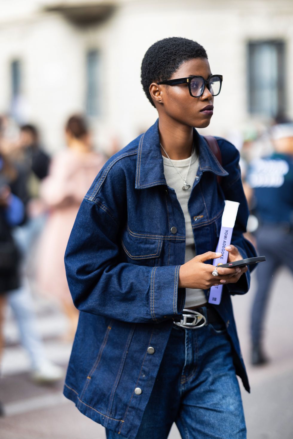 A model is seen wearing black glasses, a white tank-top, a blue jeans oversized jacket, a silver and black Diesel belt and blue jeans outside the Max Mara show during the Milan Fashion Week