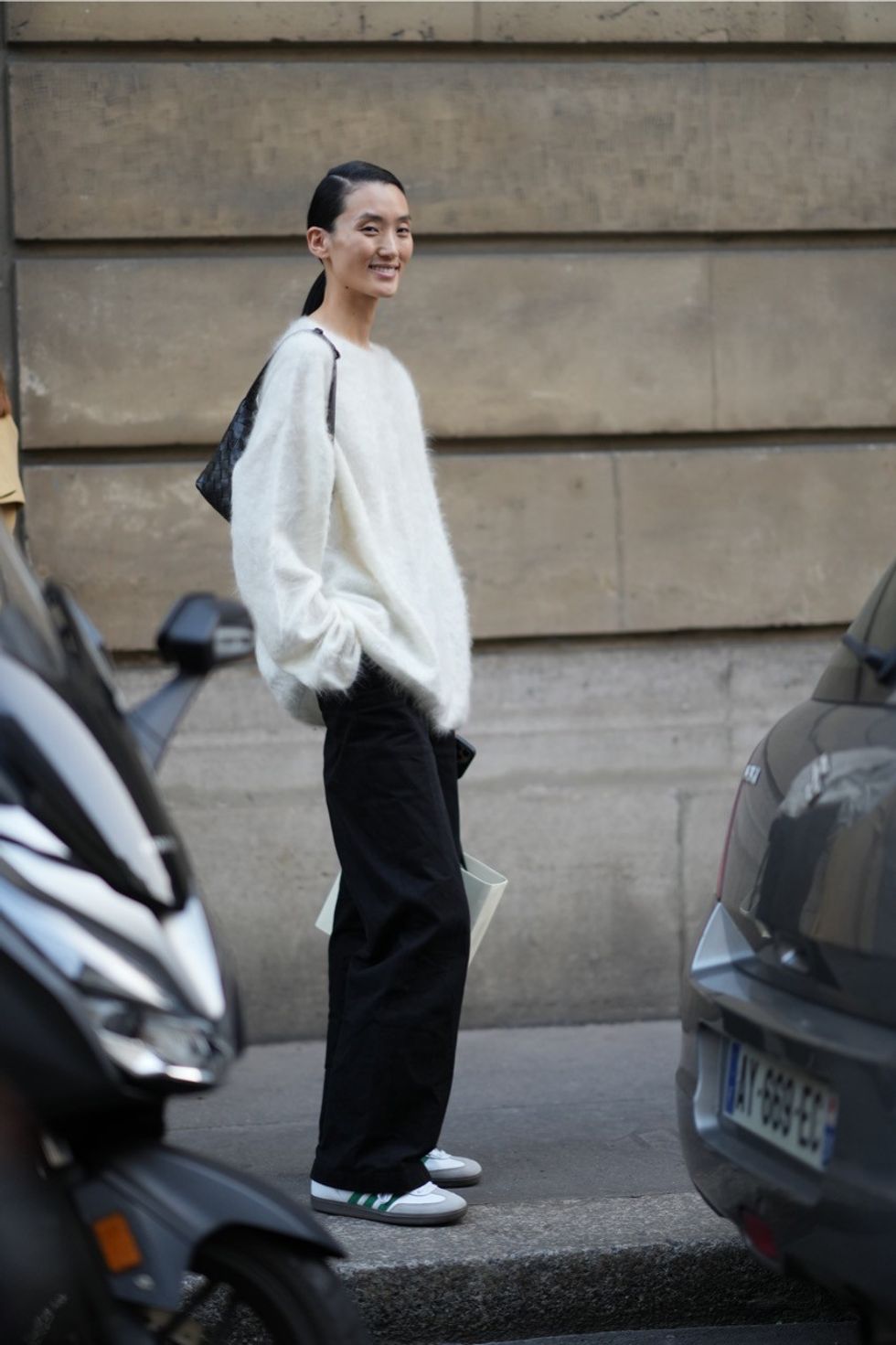 A model wears a white fluffy pullover, a bag, black flared pants, sneakers, outside Victoria Beckham, during the Womenswear Spring/Summer 2024 as part of Paris Fashion Week