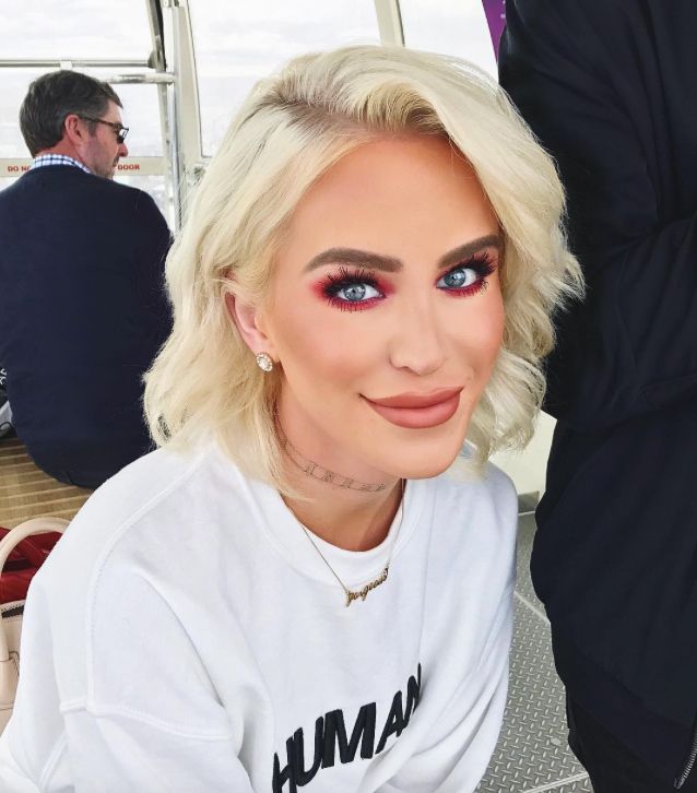 A photograph of the woman Gigi Gorgeous.  She is blonde with blue eyes, and is wearing bright red eyeshadow with neutral lipstick.