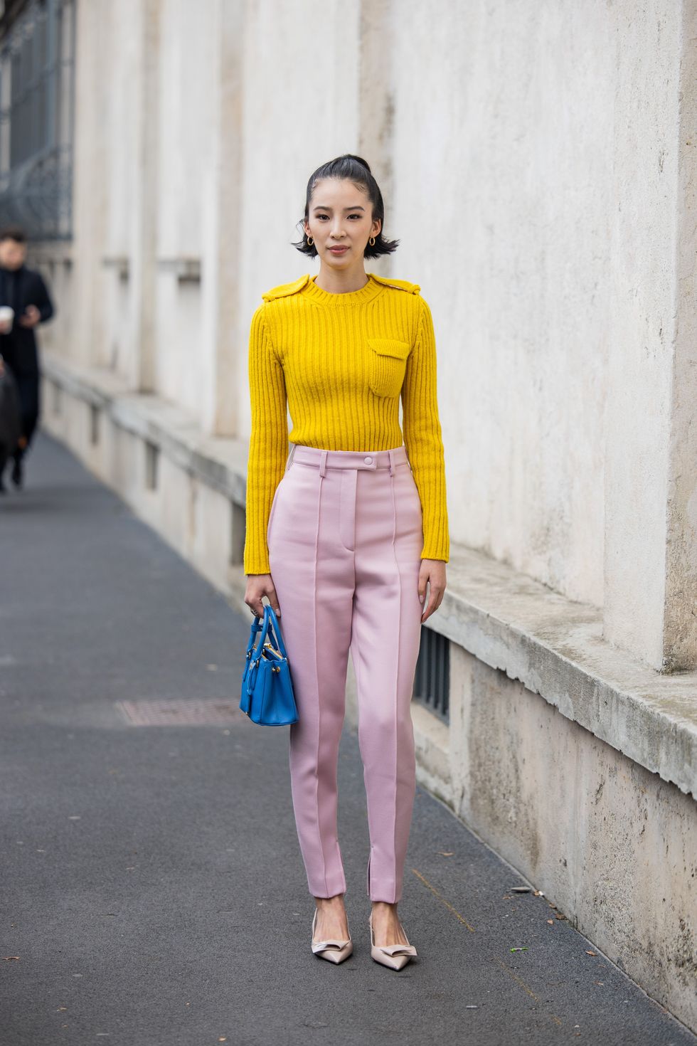 Irene Kim wears yellow knit with front pocket, pink pants, blue bag outside Prada during the Milan Fashion Week