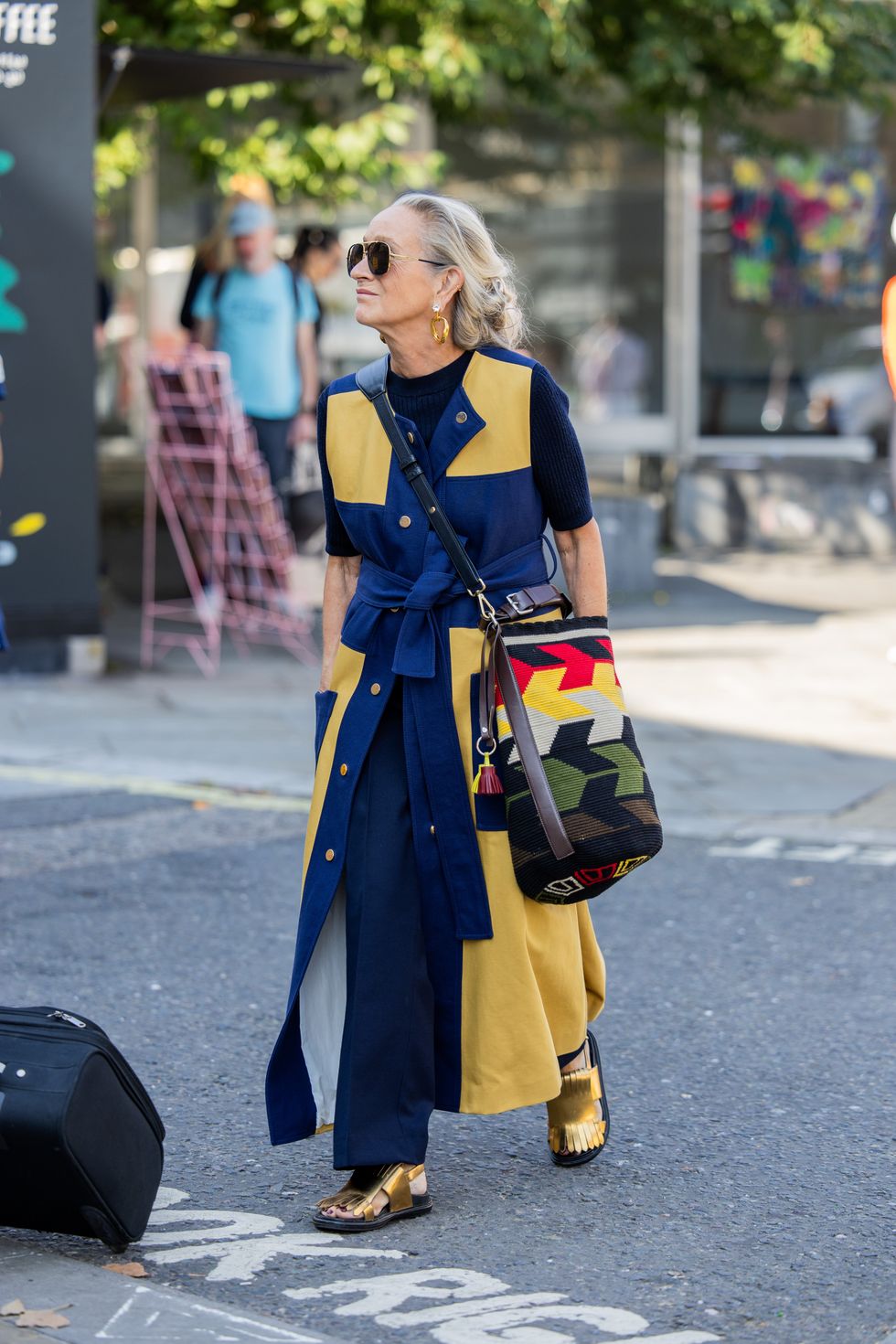 Lucinda Chambers wears navy yellow belted checkered coat, bag with pattern and color outside JW Anderson during London Fashion Week