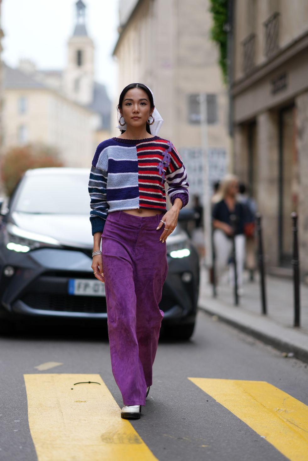 Yoyo Cao wears a white scarf over the head, earrings, a purple and blue and red striped pullover, purple velvet flared pants, outside Cecilie Bahnsen, during the Womenswear Spring/Summer 2024